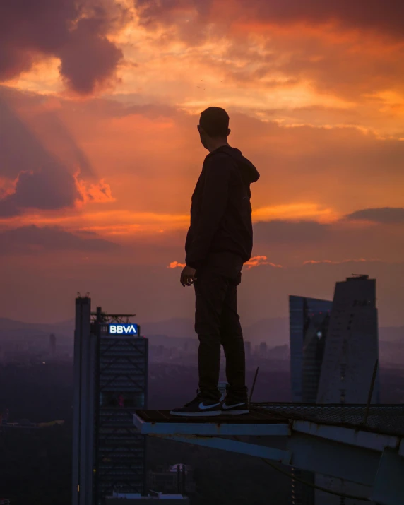 a skateboarder looks on from the edge of a skyscr