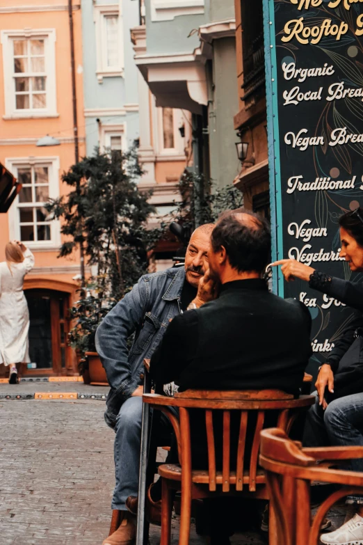 three people sitting outside with the man holding his umbrella