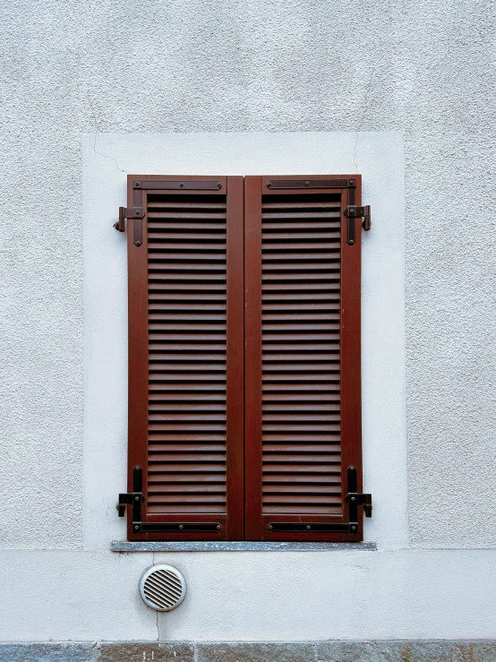 a small window with two brown wood louvereds on a white stucco wall