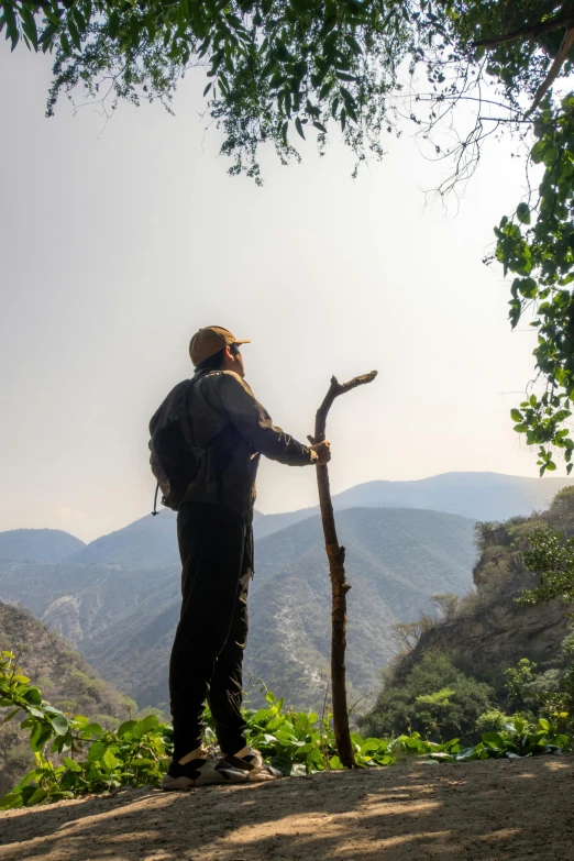 a man with a hat and backpack on standing in front of a tree