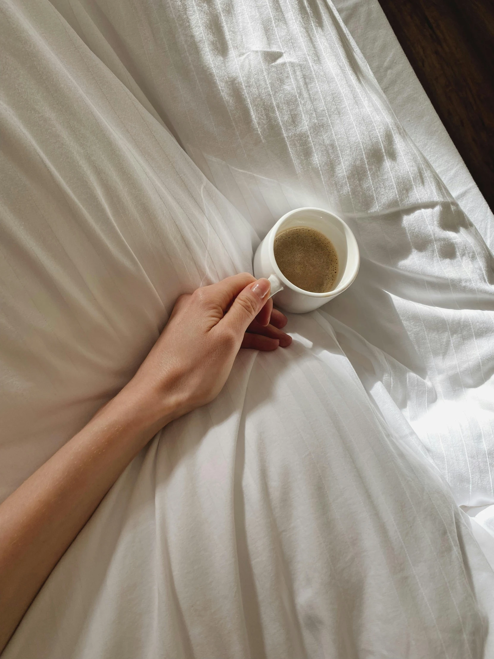 a woman laying in bed holding her cup of coffee