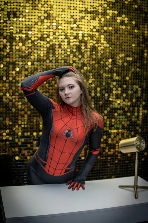 a woman wearing a red and black spider suit and posing in front of gold flecks