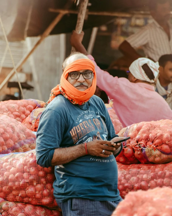 a man in a bright orange mask holding a phone while standing next to a pile of produce