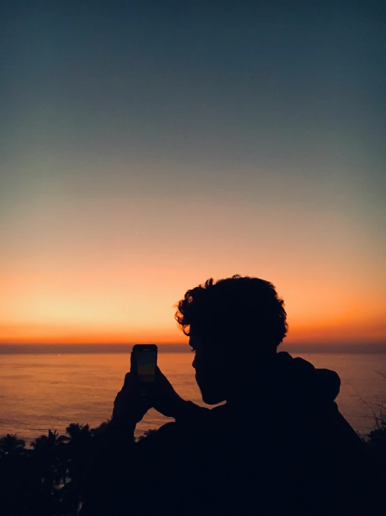 a woman holding up her phone taking pictures at sunset