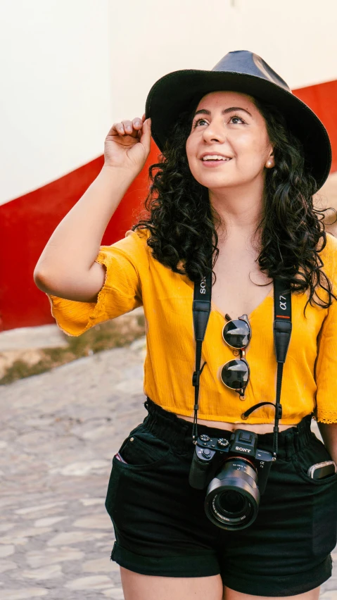 a young woman with long hair wearing black shorts and a yellow shirt, holding up her camera