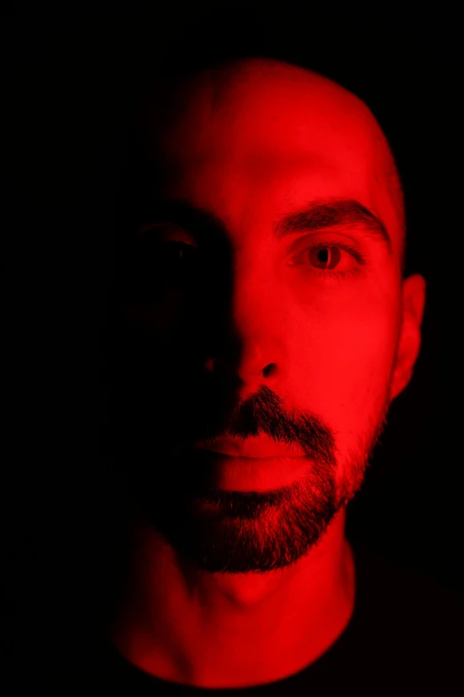 a man with short hair and beard standing in a dark room