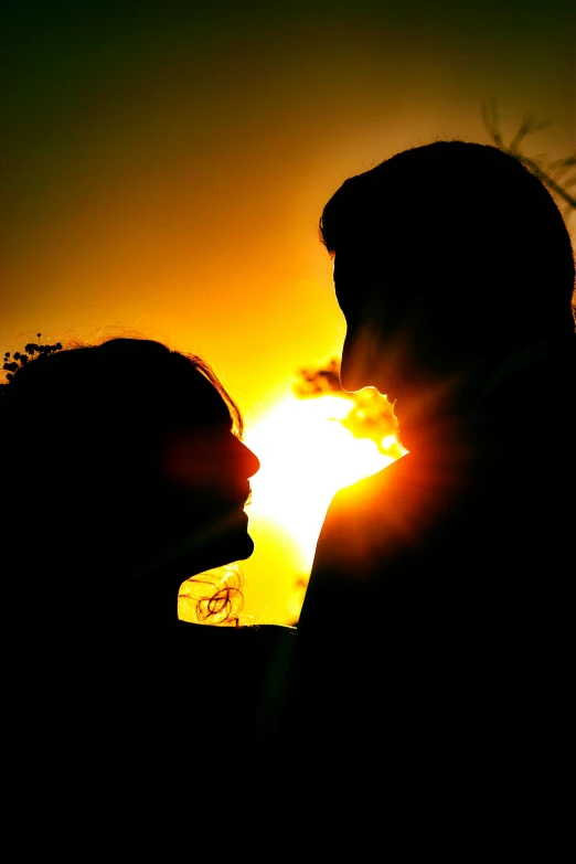 man and woman kissing while sun goes down on horizon