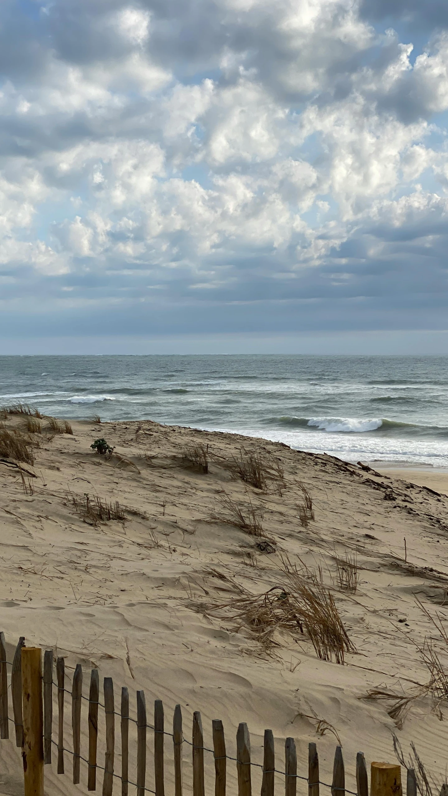 the clouds cover the sky over the beach with a wooden fence