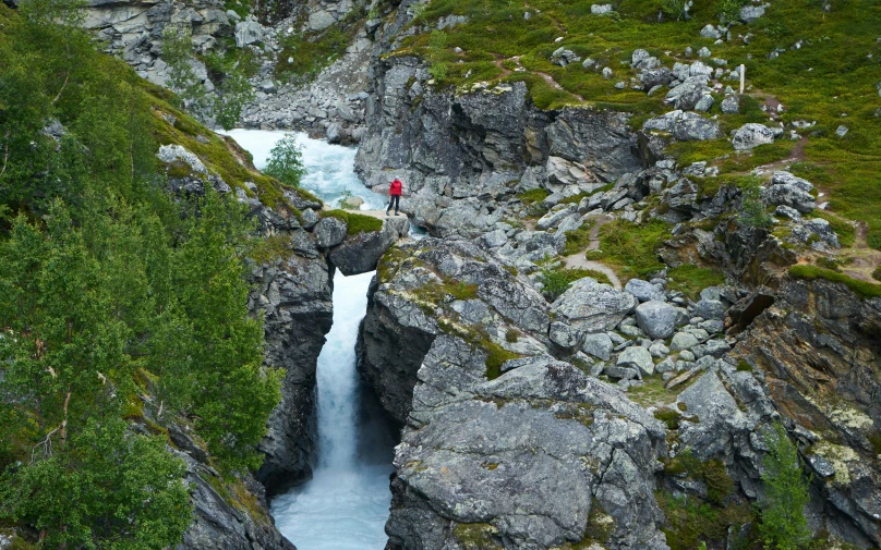 person standing in large rocky area with waterfall in foreground