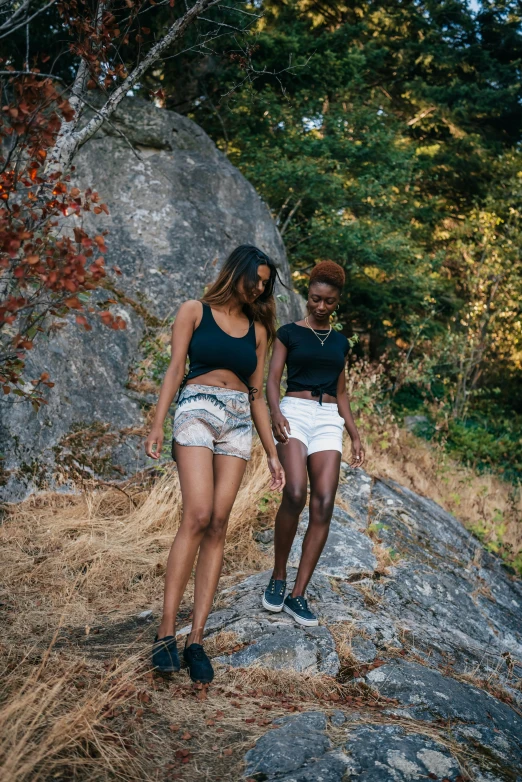 two beautiful women in white shorts and black shirts standing on top of a rock