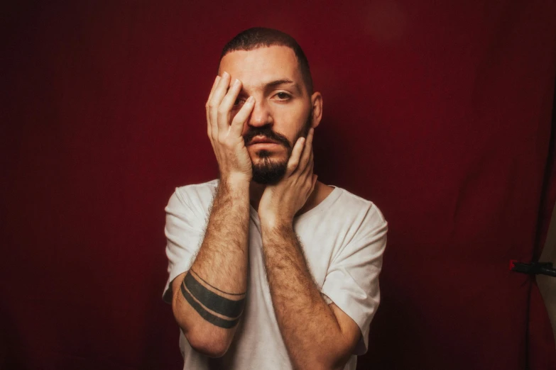 a man holding his hands near his face with red wall behind