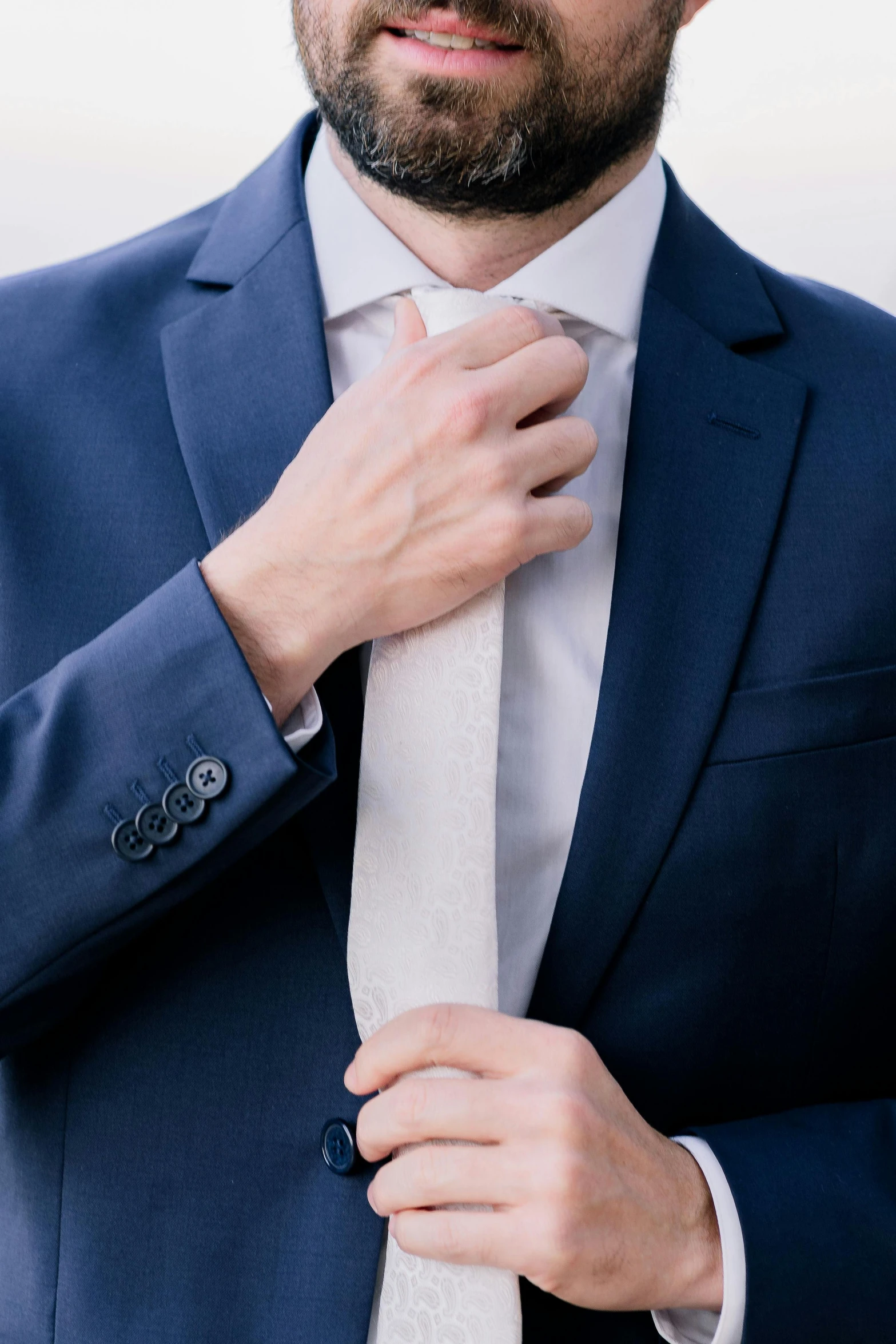 the man wearing a blue suit and tie adjusts his bow tie