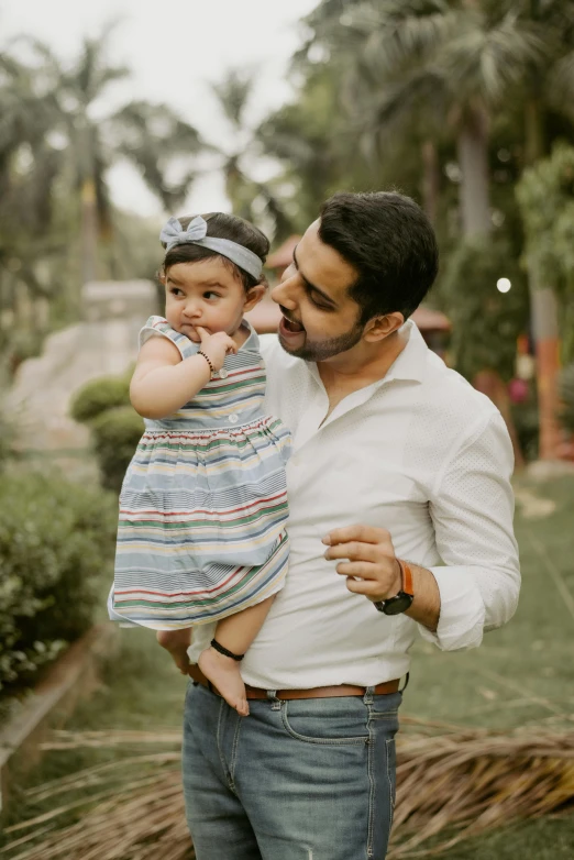 a father holding his baby girl while smiling at the camera