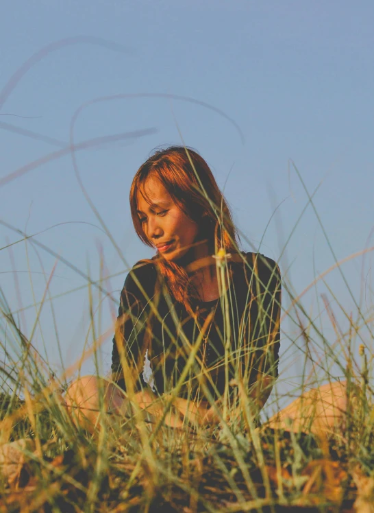 a woman sitting in tall grass looking at her cell phone