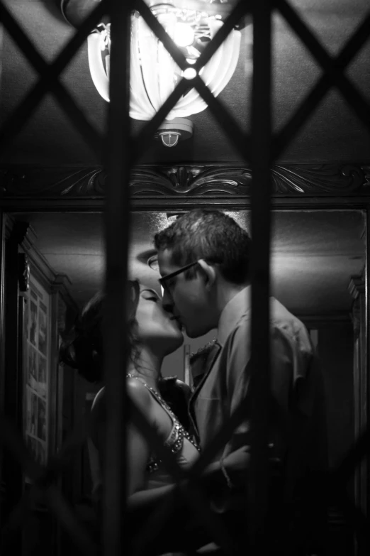 a man kisses a woman while looking at her reflection through bars in a mirror
