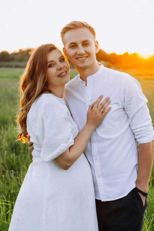 a couple smile at the camera while in a field