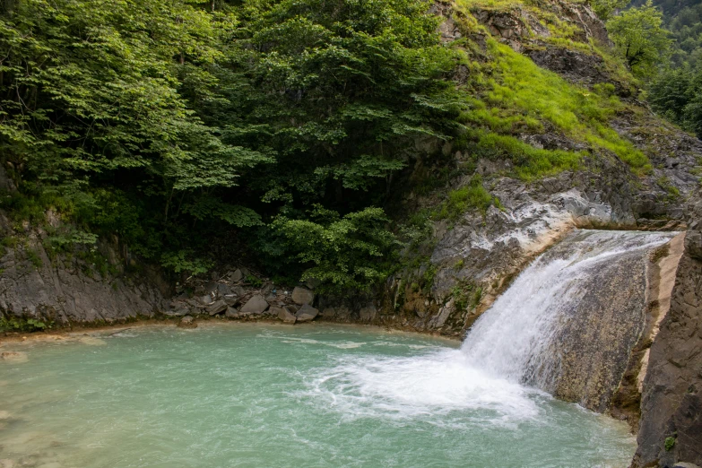 waterfall on side of river with people jumping into it