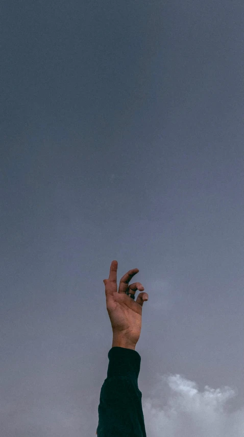 hand reaching up into sky towards cloudy sky