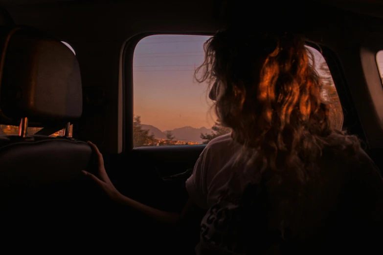 a woman looking out the window of a vehicle at the setting sun