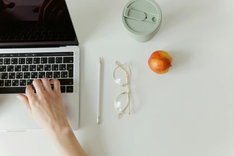 a person on a white laptop next to glasses and an orange