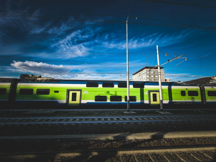 green train traveling past a station with blue sky in the background