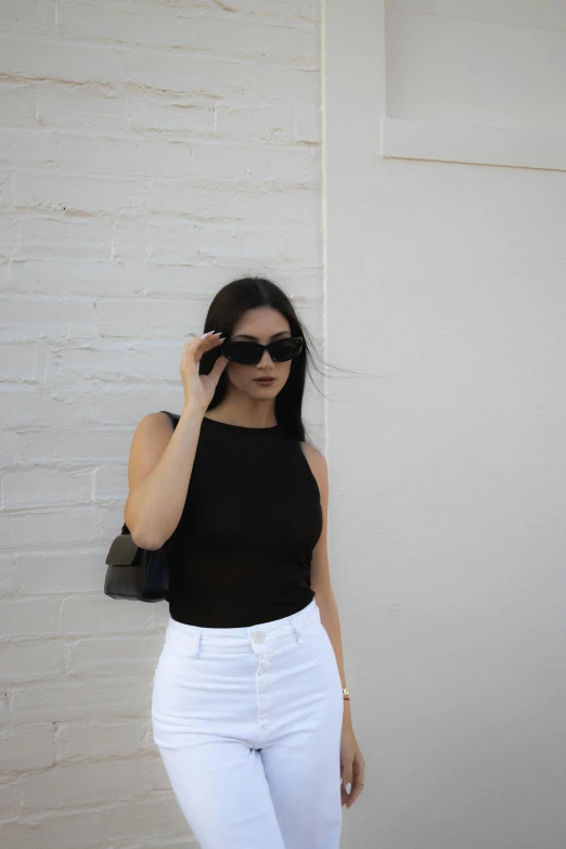 a young woman wearing sunglasses is leaning against a white wall