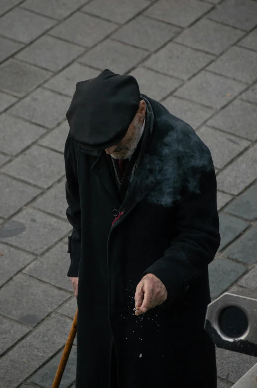 an older man in black coat and hat walking down the street