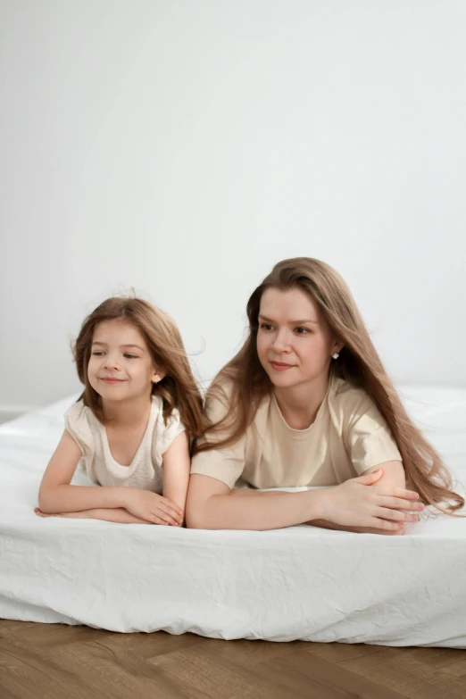 a woman sitting next to a little girl on a bed