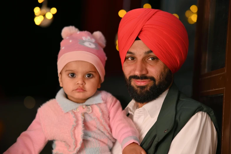 a man holding a child wearing a pink turban