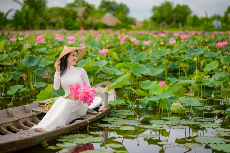 a woman sitting in a small boat in the water with pink flowers