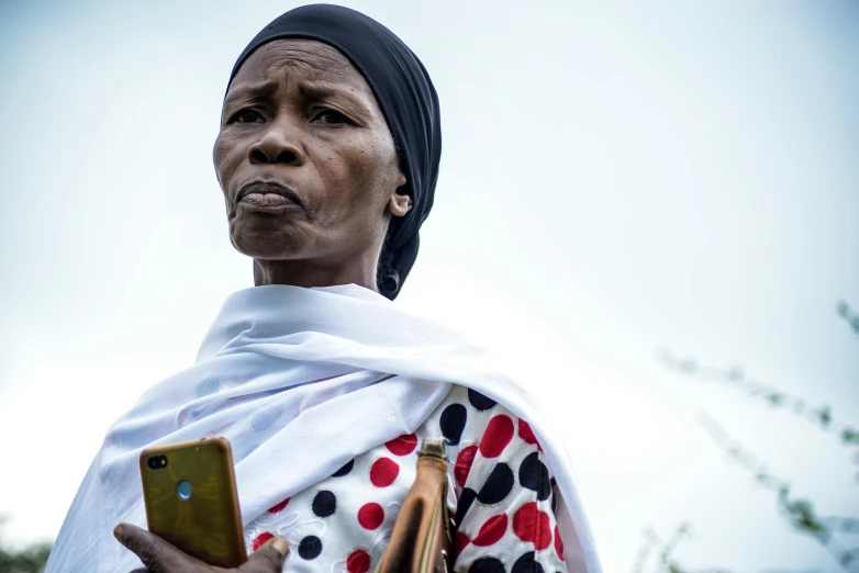 a woman holds her cell phone and stares into the camera