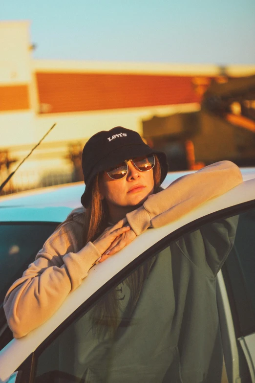 a woman in black hat and sunglasses with hand on her hips leaning out of car