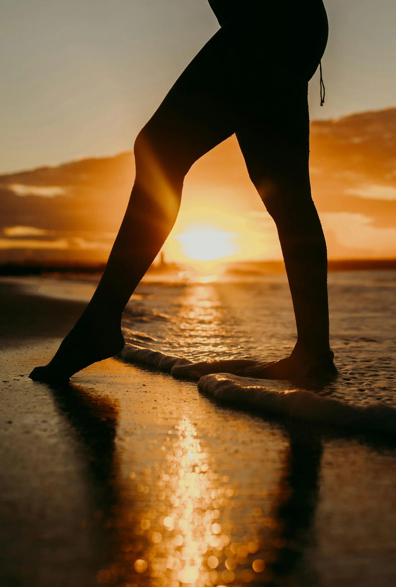 the person is walking along the sand at sunset