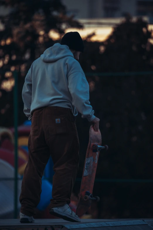 a man in a hoodie stands with his skateboard