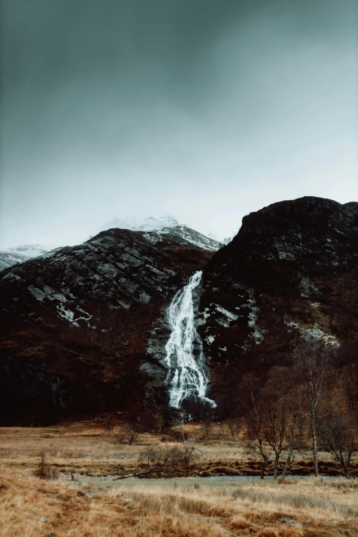 a snowy mountain with a waterfall and a tree