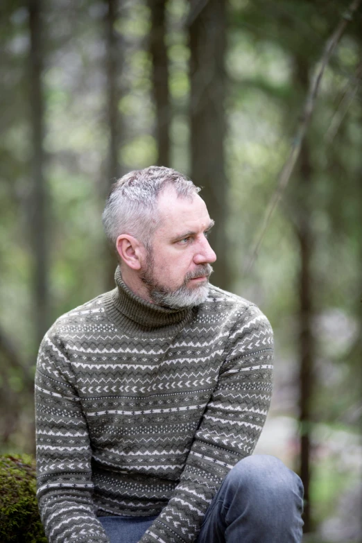 a man sitting in the woods wearing a sweater