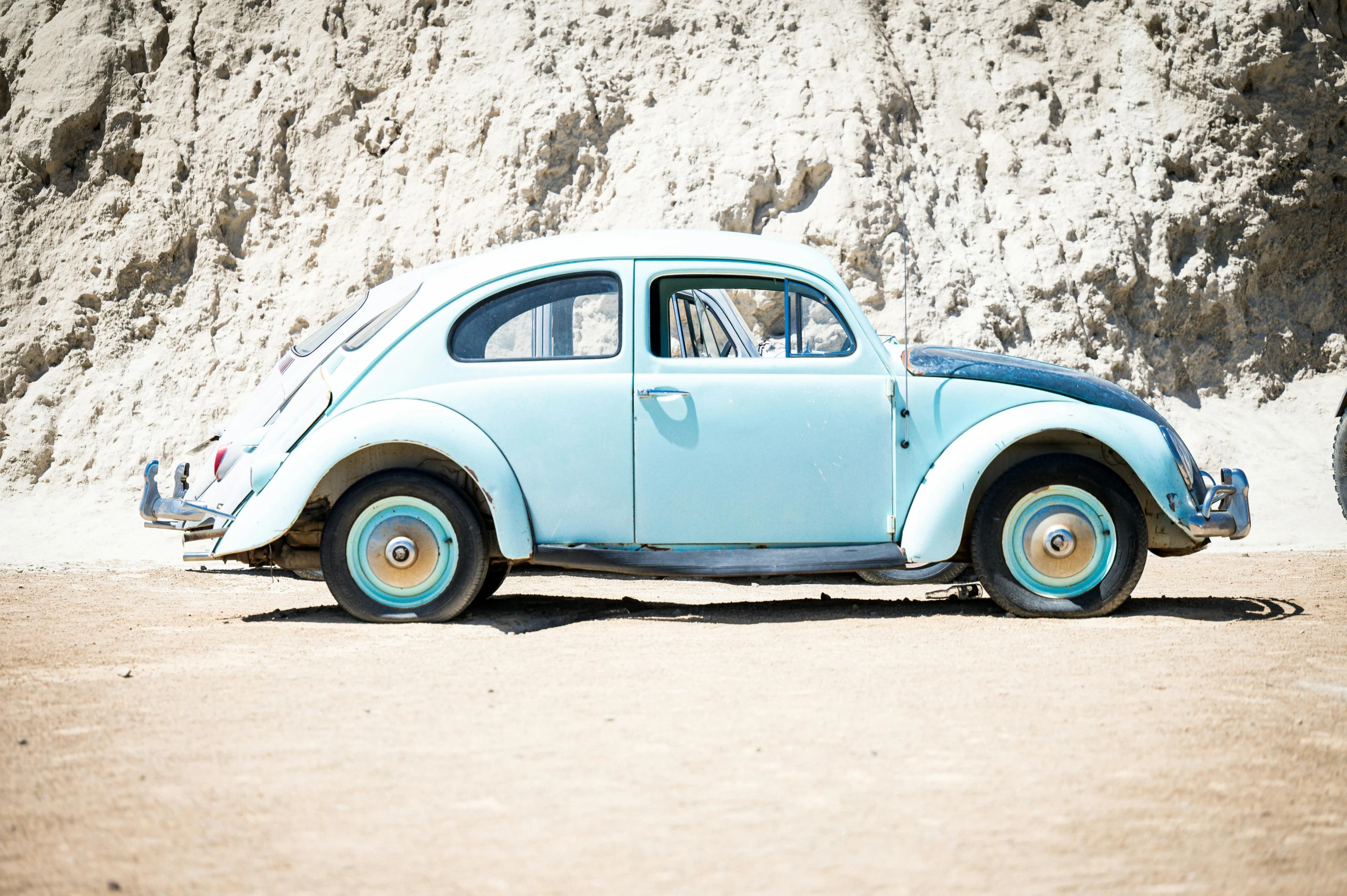 blue volkswagen car with wheels parked in front of cliff