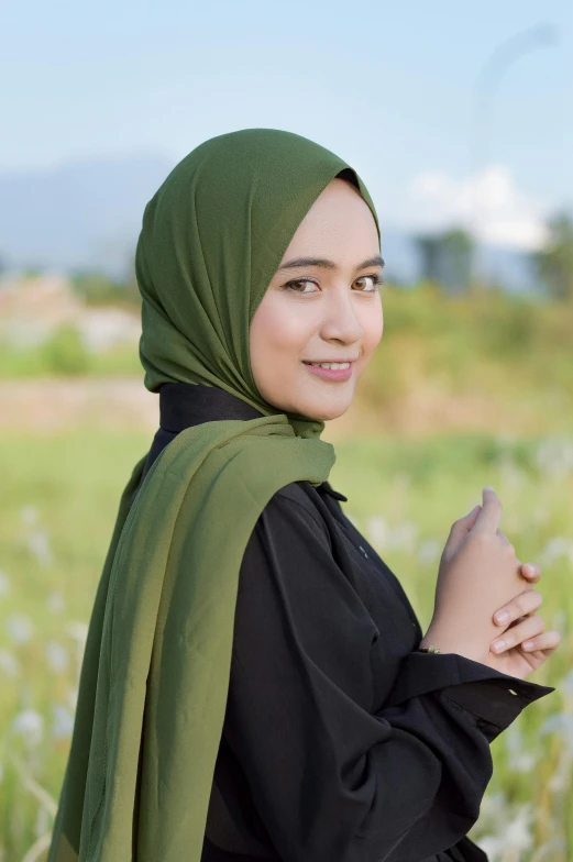 a girl in a green hijab smiles as she stands outside