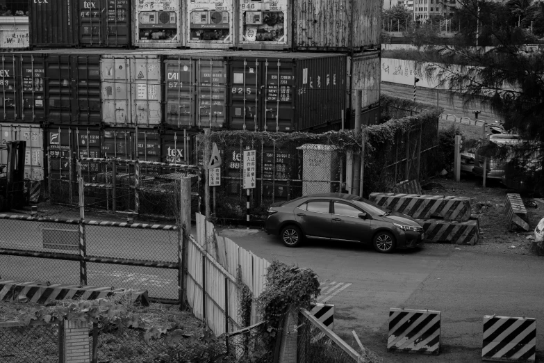 the small car is parked by the many shipping containers