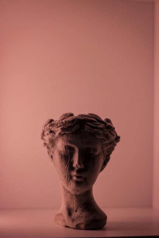 a ceramic face in front of a pink wall