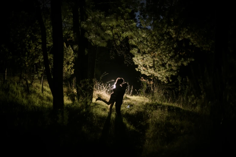 two people stand in the woods at night, arms around each other