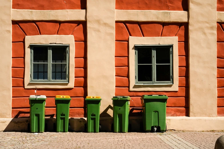 three trashcans are side by side in front of a brick building