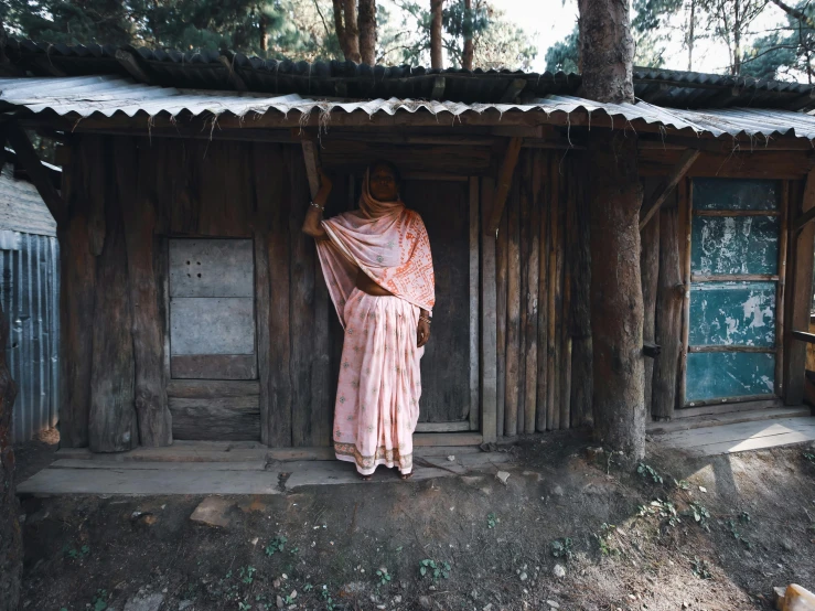 a woman wearing a pink dress standing outside a wooden house