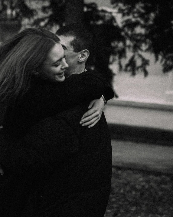 two people, one in black, are hugging each other