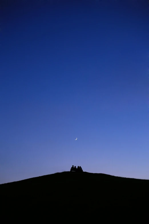 a couple of people walking across a field under the moon