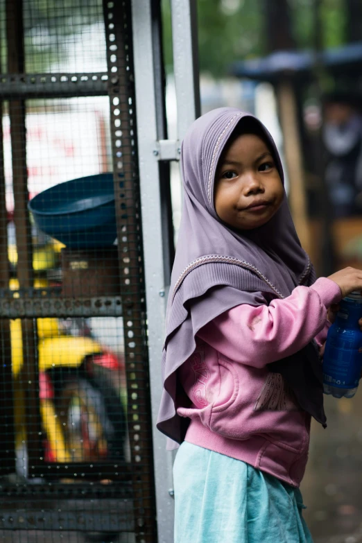 the little girl is wearing a purple hijab and drinking from a blue can
