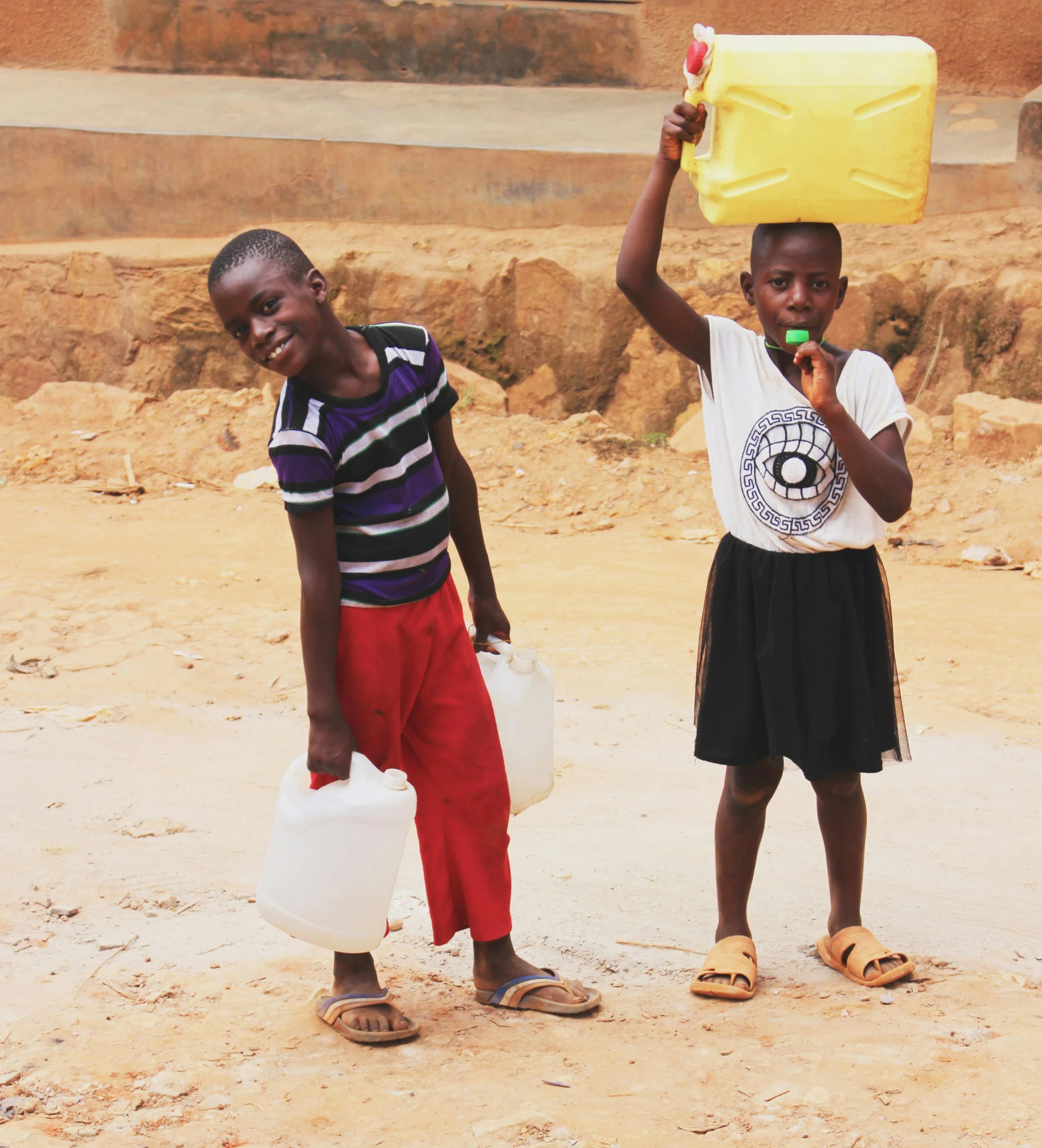 two s standing together holding onto plastic jugs and an oil can