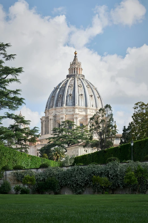 a dome building stands tall behind hedges on a cloudy day