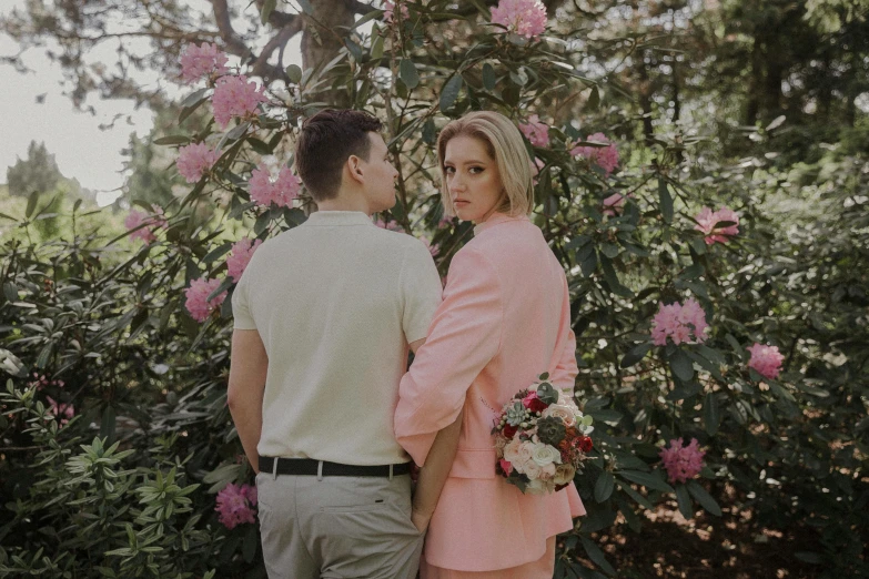 a couple stands in front of flowering bush looking at each other