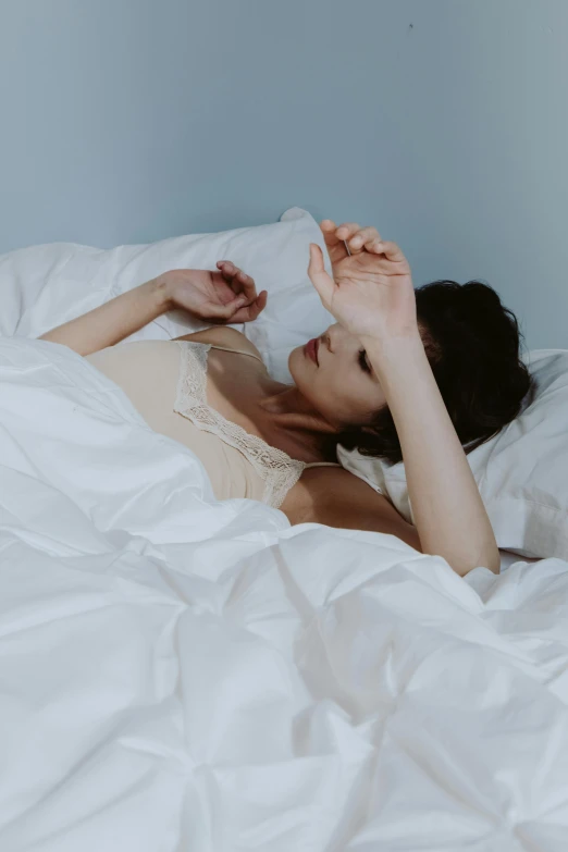 a woman lays in bed with white sheets on her
